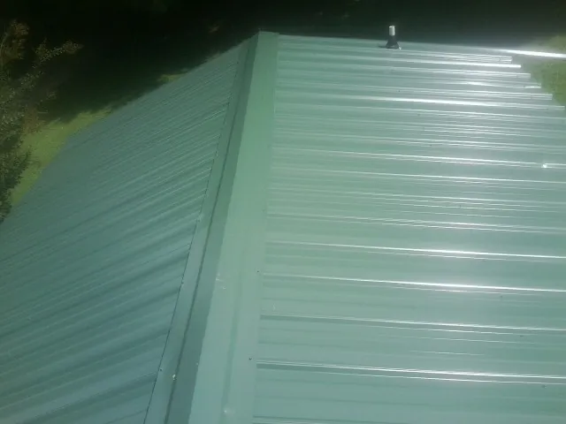 New green metal panels meeting at the ridge of a roof — Flat Roof Repair work by our crew in Coats