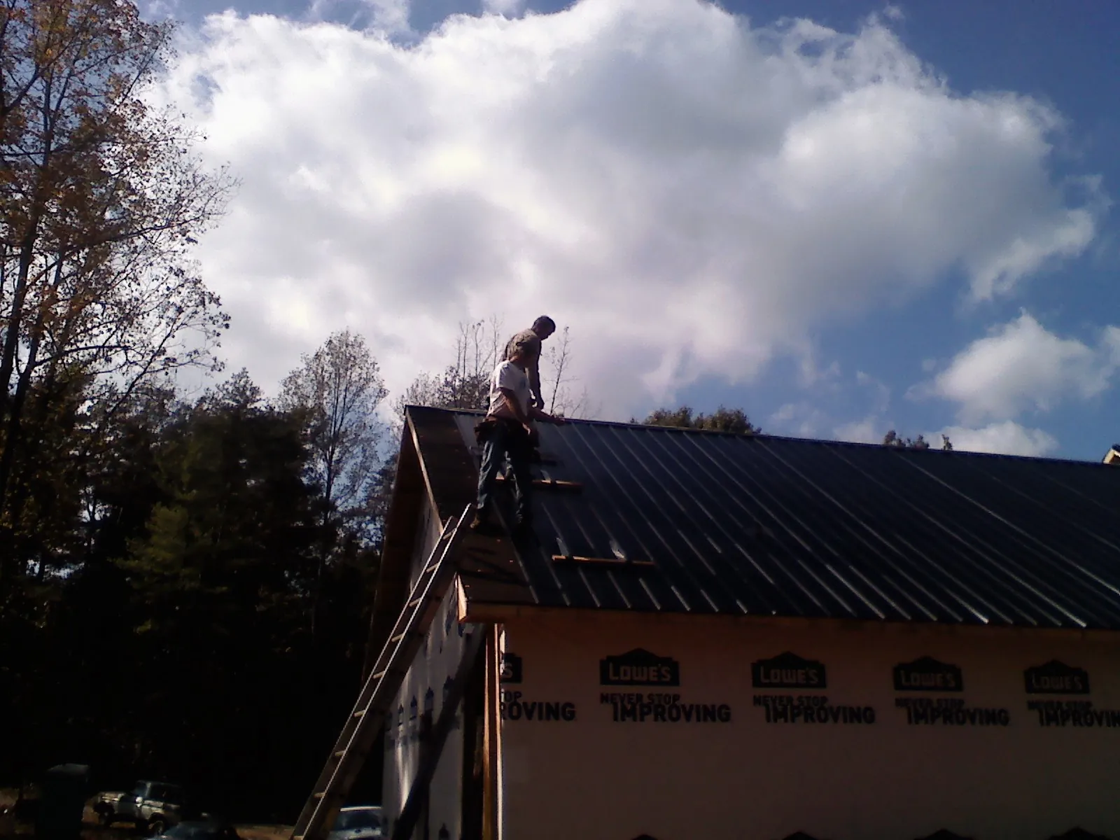 Roofer fastening dark metal panels high against a cloudy sky, from a Roof Inspection job in Coats